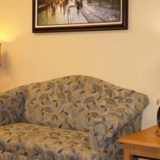 A cozy living room corner featuring a patterned sofa, a wall-mounted artwork, a warm lamp, and a small wooden table.