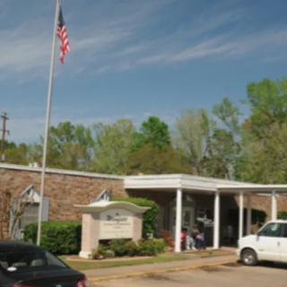 A small brick building with an American flag in front, surrounded by trees and parked cars under a clear sky.