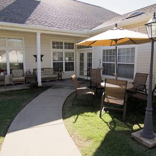 A cozy outdoor patio area with chairs and a large umbrella, connected by a paved pathway to the house.