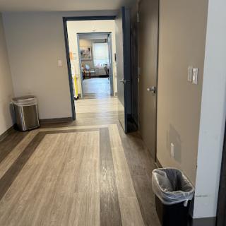 A modern office hallway featuring wooden flooring and a trash can.