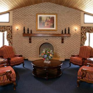 A cozy living room with a brick fireplace, surrounded by striped armchairs and a wooden coffee table.
