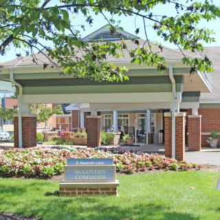 A welcoming building entrance with an awning and well-maintained landscaping featuring flowers and a tree.