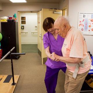 A healthcare professional assists an elderly man during a physical therapy session.