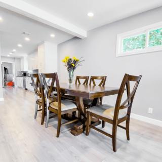 A modern dining room with a wooden table and chairs, complemented by bright lighting and a vase of flowers.