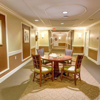 A well-lit hallway featuring a round table surrounded by chairs, with wall art and carpeted flooring.