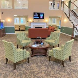 A cozy living room with a seating area including green chairs and a coffee table, featuring a carpeted floor, a television, and a staircase.