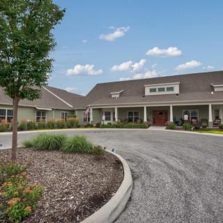 A landscaped driveway leads to a modern single-story building under a blue sky with clouds.