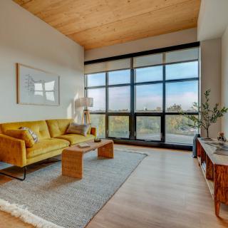A modern living room with a yellow sofa, wooden ceiling, and large windows that bring in natural light.