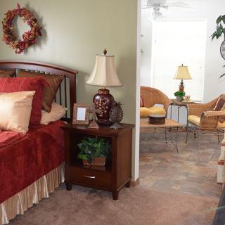 A cozy bedroom with a nightstand and lamp, leading into a living room area with seating.