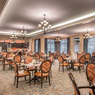 An elegant dining room with several tables and chairs, featuring chandeliers and a carpeted floor.