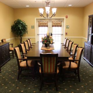 A well-lit dining room with a long table and elegant chairs, adorned with a central floral arrangement.