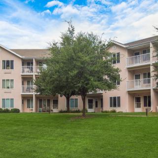 A multi-story residential apartment building with balconies, surrounded by a lush green lawn and trees.