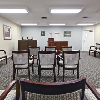 A small chapel room with arranged seating and a cross at the front.