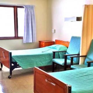 A hospital room with two beds and chairs.