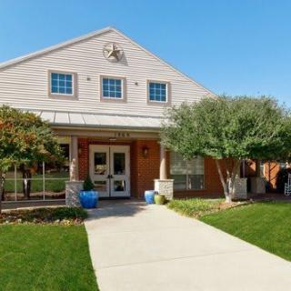 A single-story residential building with a landscaped front garden and a concrete sidewalk leading to the entrance.