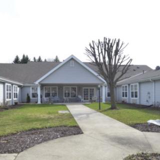 A residential building with a pathway leading to the entrance, surrounded by a lawn and trees.