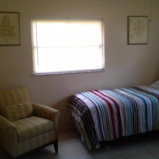 A cozy bedroom featuring a single bed with a striped blanket and an armchair by the window.