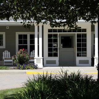 A quaint house with a porch and chairs surrounded by greenery.