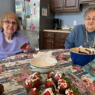 Two elderly women enjoy preparing desserts at a kitchen table.