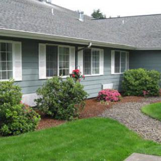 A well-maintained front yard with a green lawn and neatly arranged shrubs in front of a house.