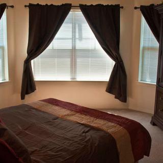 A cozy bedroom with a neatly made bed and large windows adorned with dark curtains.