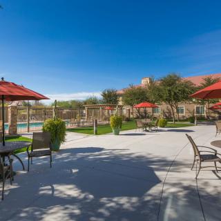 A sunny outdoor patio area with tables, chairs, umbrellas and a nearby pool.