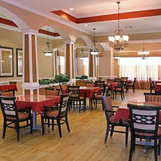 An elegantly designed dining area with red tablecloths, chandeliers, and wooden flooring, featuring decorative columns.