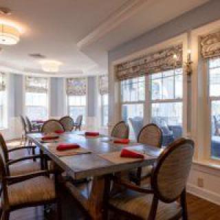 A well-lit dining room with a large table and neatly arranged chairs, accented by natural light streaming through the windows.