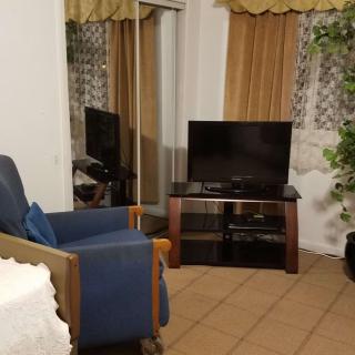 A cozy living room with a television, blue chair, and golden curtains.