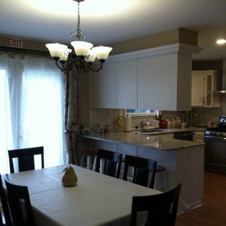 A cozy dining area adjacent to a modern kitchen, featuring a table set with chairs and illuminated by a chandelier.