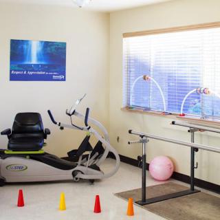 A therapy room equipped with a stationary bike, exercise ball, and training cones.