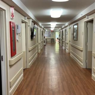 A long, well-lit corridor with wooden flooring and multiple doors.