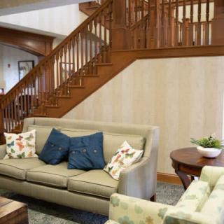 A cozy living room featuring a beige sofa with decorative pillows, a wooden staircase, and a round coffee table.