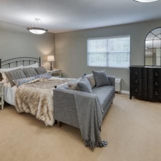 A spacious bedroom with a large bed, a sofa at the foot of the bed, and a dresser by the window.