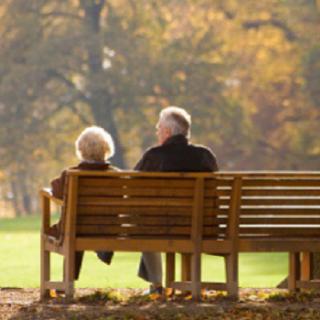An elderly couple sits on a bench in a park, enjoying the autumn scenery.