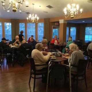 A group of seniors enjoying a meal together in a warmly lit dining hall.