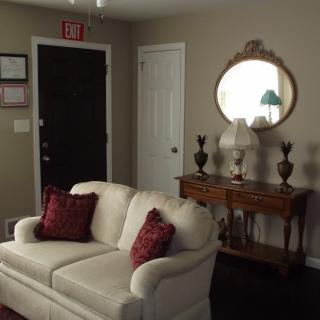 A cozy living room with a white sofa and decorative red cushions, complemented by a wooden table and a round mirror.