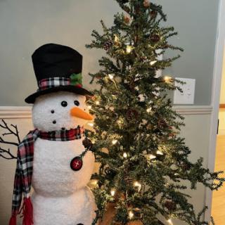 A cheerful snowman stands beside a beautifully lit Christmas tree, celebrating the festive season.