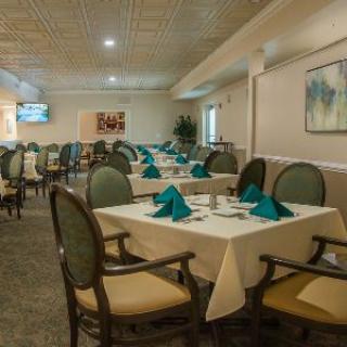 An elegantly arranged dining area with neatly set tables and chairs, featuring teal napkins and framed artwork on the walls.