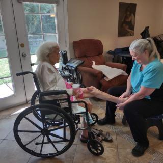 An elderly woman in a wheelchair interacting with a caregiver indoors.