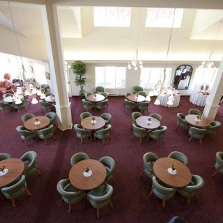 An empty restaurant dining area with round tables and chairs on a carpeted floor.