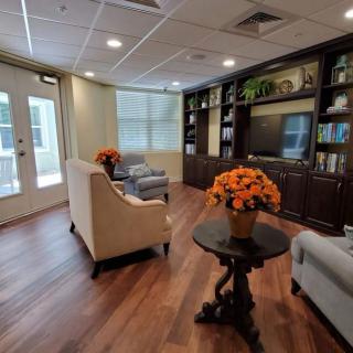 A cozy living room with elegant furniture, wood flooring, and decorative bookshelves adorned with potted plants.