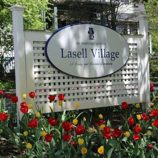 A Lasell Village sign surrounded by vibrant red and yellow tulips in a garden setting.