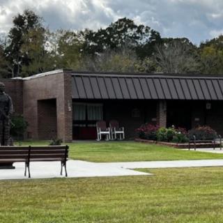 A small brick building surrounded by a grassy lawn and benches, with trees and a cloudy sky in the background.