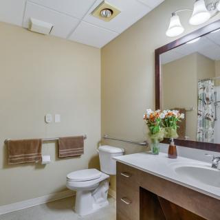 A modern bathroom with a toilet, sink, and large mirror, featuring towels and decorative flowers.