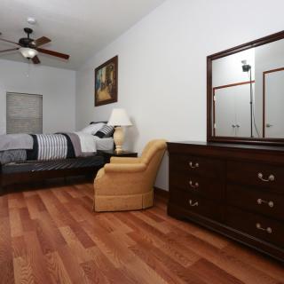 A neatly arranged bedroom featuring a bed, dresser with mirror, and chair on hardwood flooring.