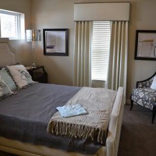 A cozy, well-decorated bedroom featuring a neatly made bed, framed artwork, and elegant curtains.