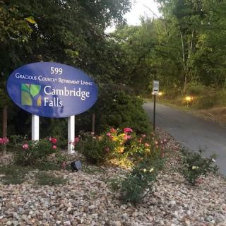 Entrance sign to Cambridge Falls with a landscaped pathway and flowers.