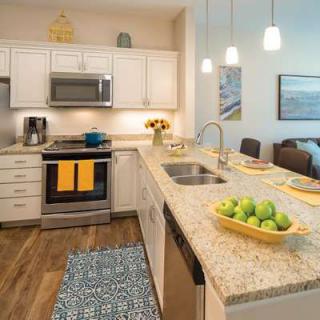 A modern kitchen interior featuring white cabinets, stainless steel appliances, and a granite countertop with a fruit bowl.