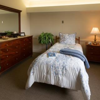 A cozy bedroom with a single bed, dresser, and lamp.